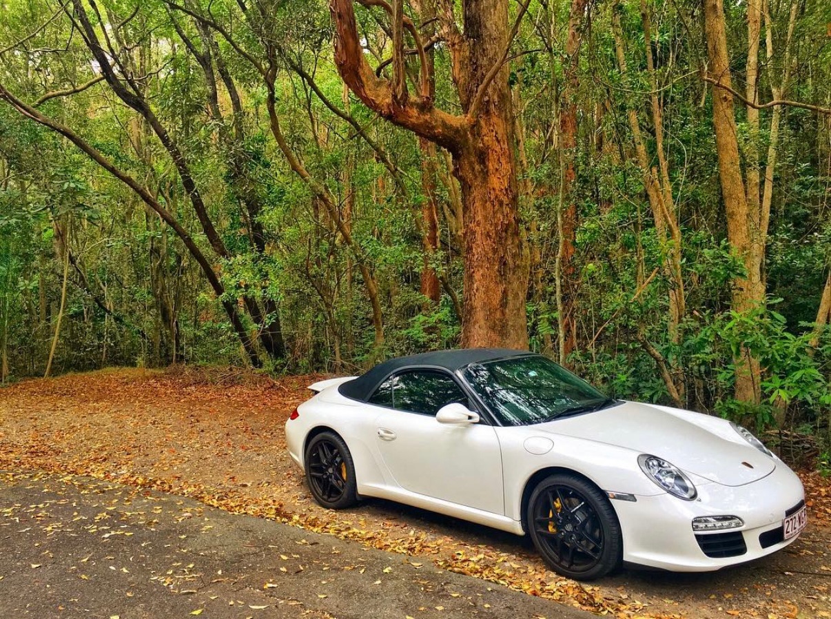A white Porsche on a wooded road