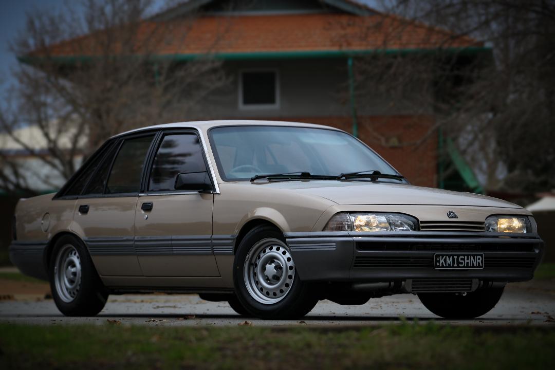 Front three-quarter beige Holden sedan outside brick building