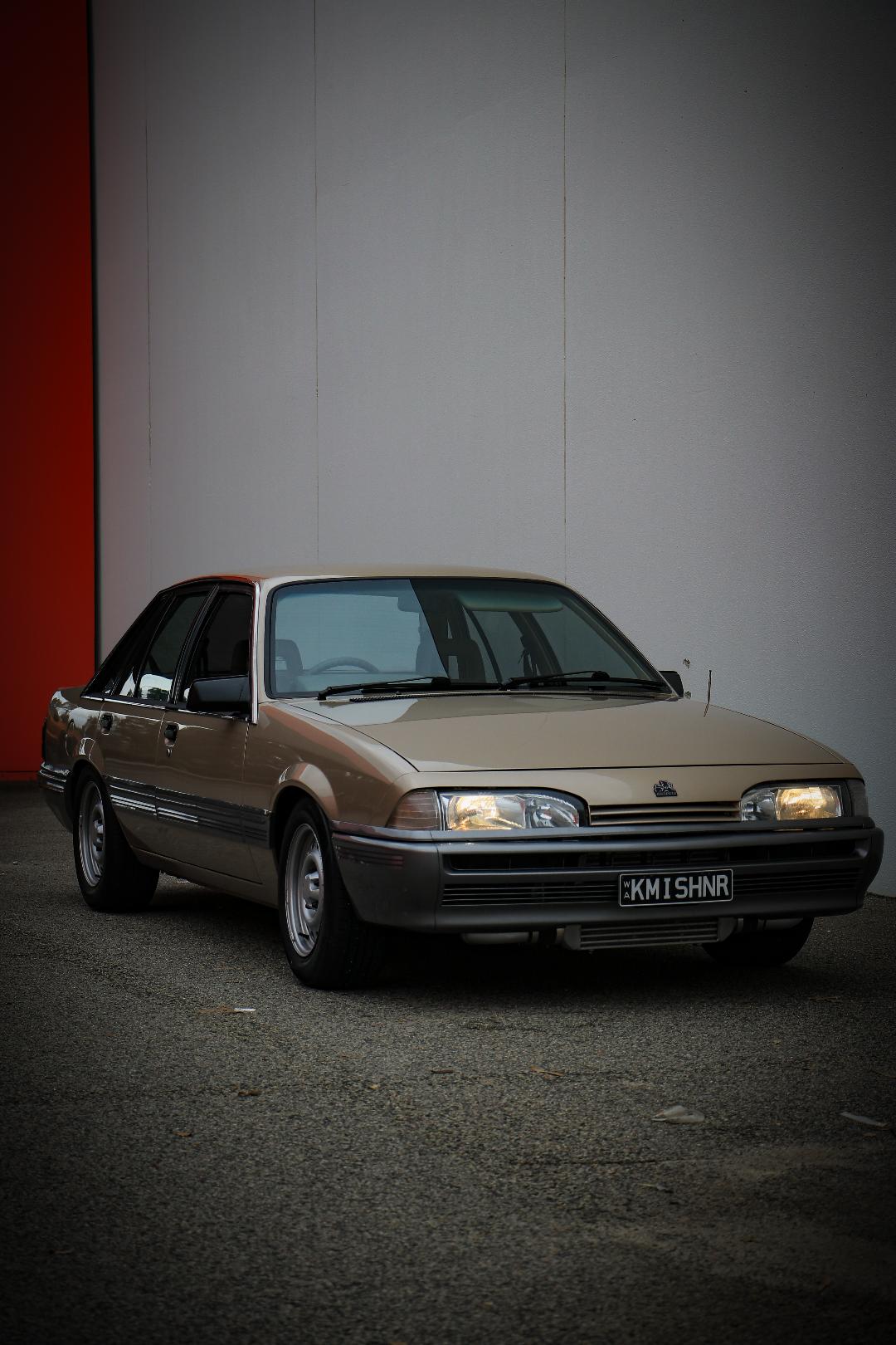 Portrait front three-quarter beige Holden sedan against wall