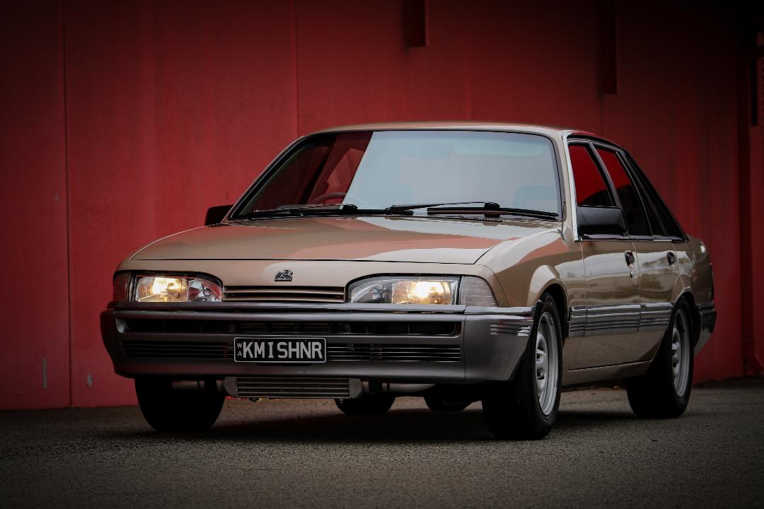 Front three-quarter beige Holden sedan against red wall
