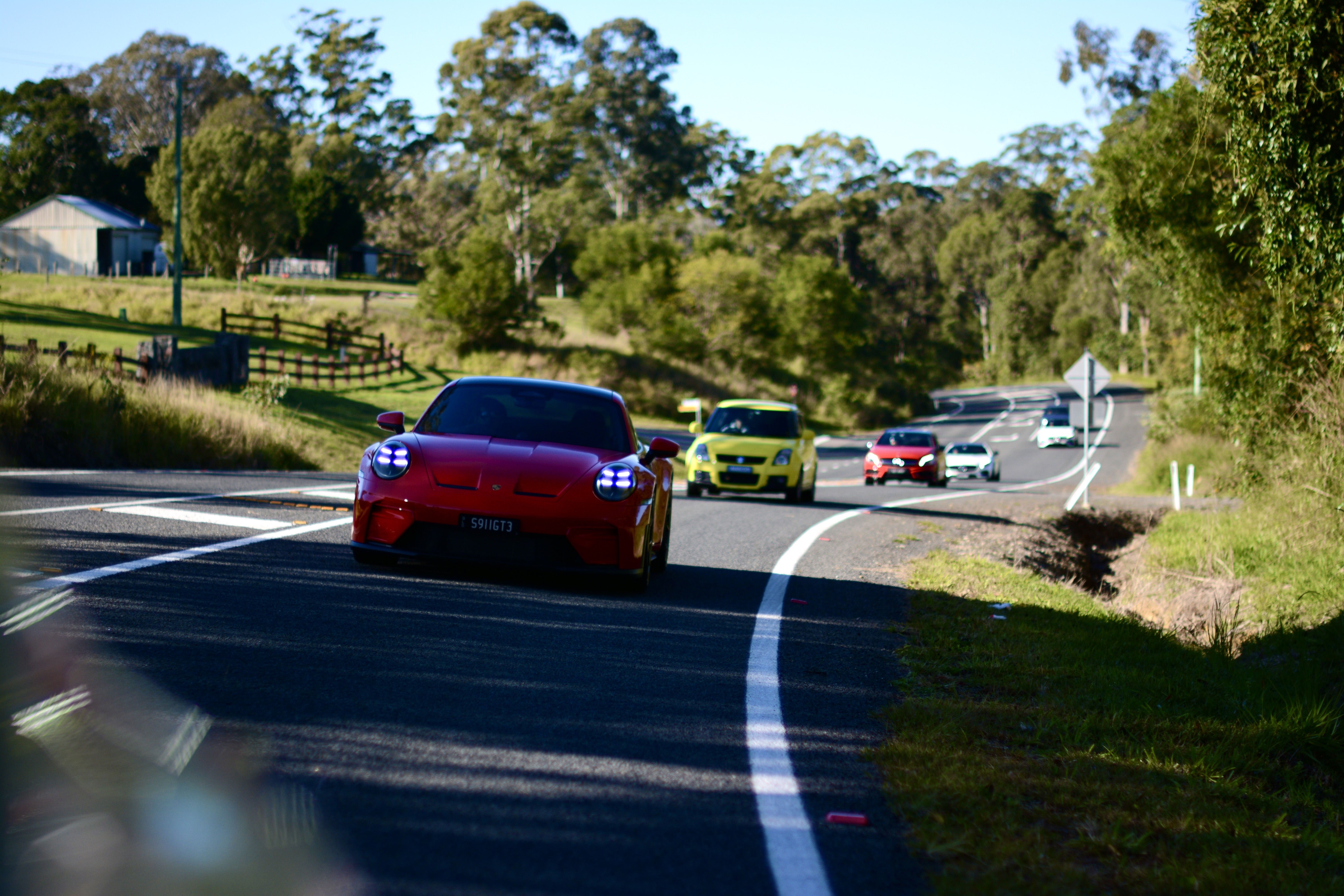 A red Porsche leading a varied group of cars along a country road
